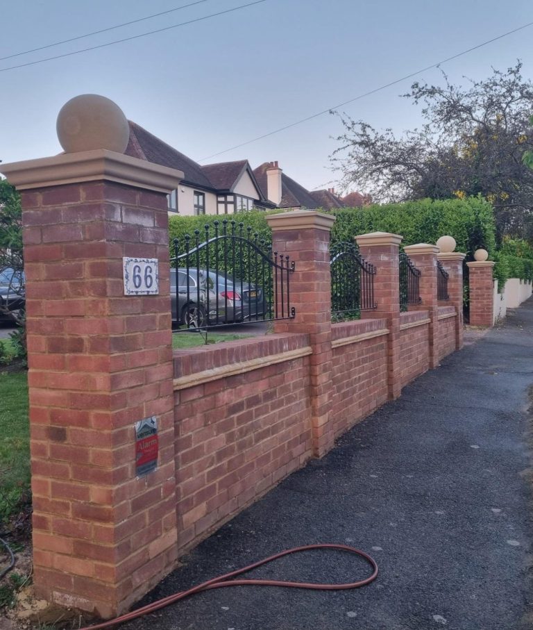 Front Brickwork Wall Brick wall with pillars and a gate, lined along a paved pathway in a residential area.